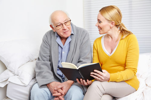 Frau liest einem alten Mann im Seniorenheim ein Buch vor