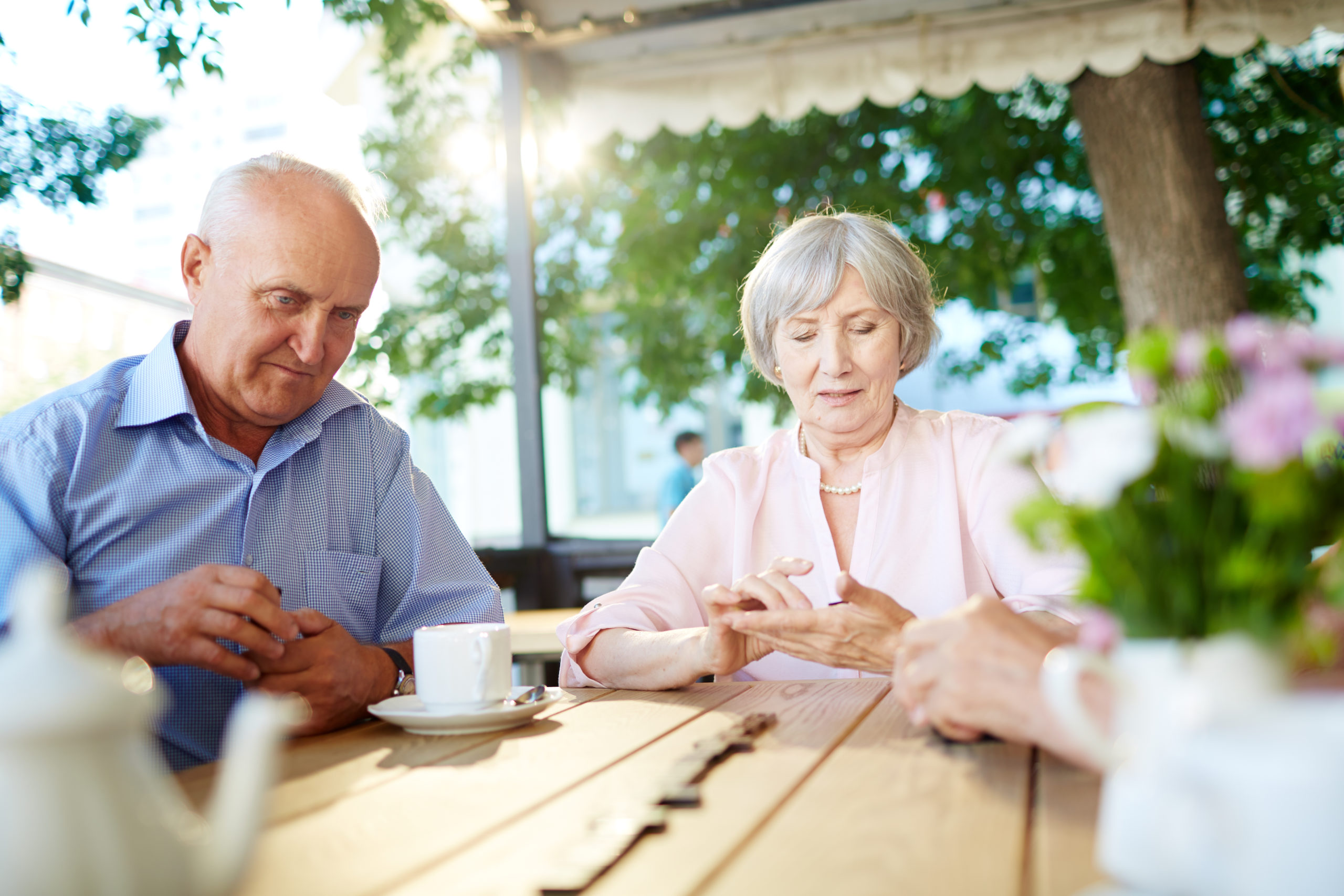 Waist-up portrait of male and female elderly people sitting at wooden table, drinking coffee and playing dominoes